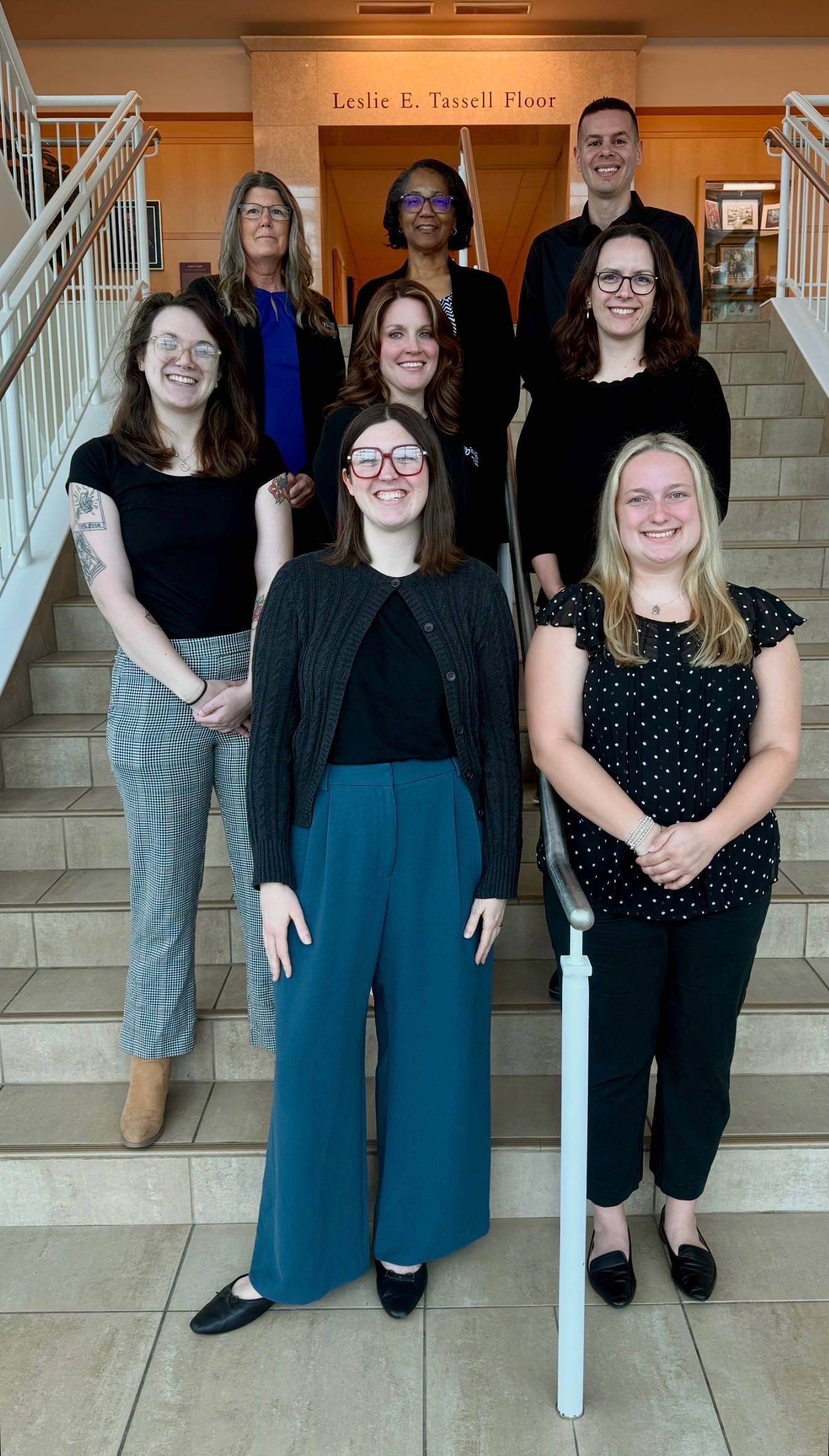 team members from the college of health professions student services office stand on a stairwell smiling at the camera